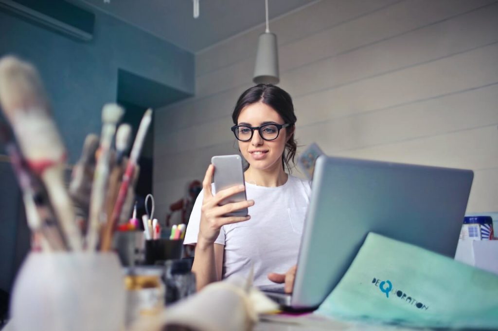 Woman looking at her phone with her laptop in front of her