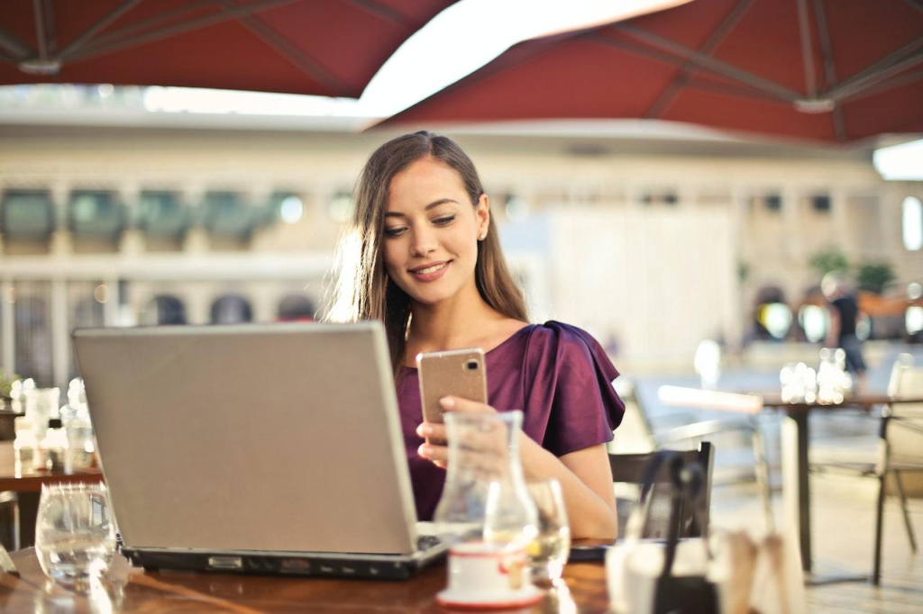 Woman sitting in a cafe looking at her phone with her laptop on the table