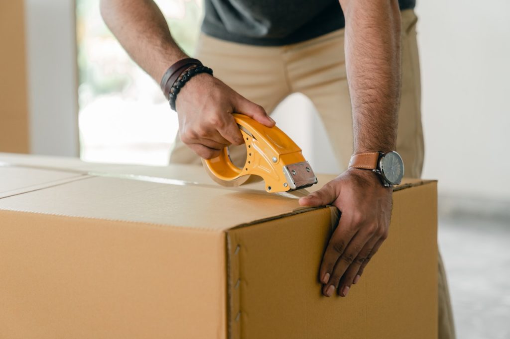 Man wrapping a cardboard box with tape.