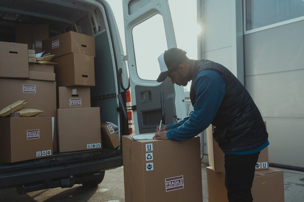A delivery man writing on paper at the back of a van