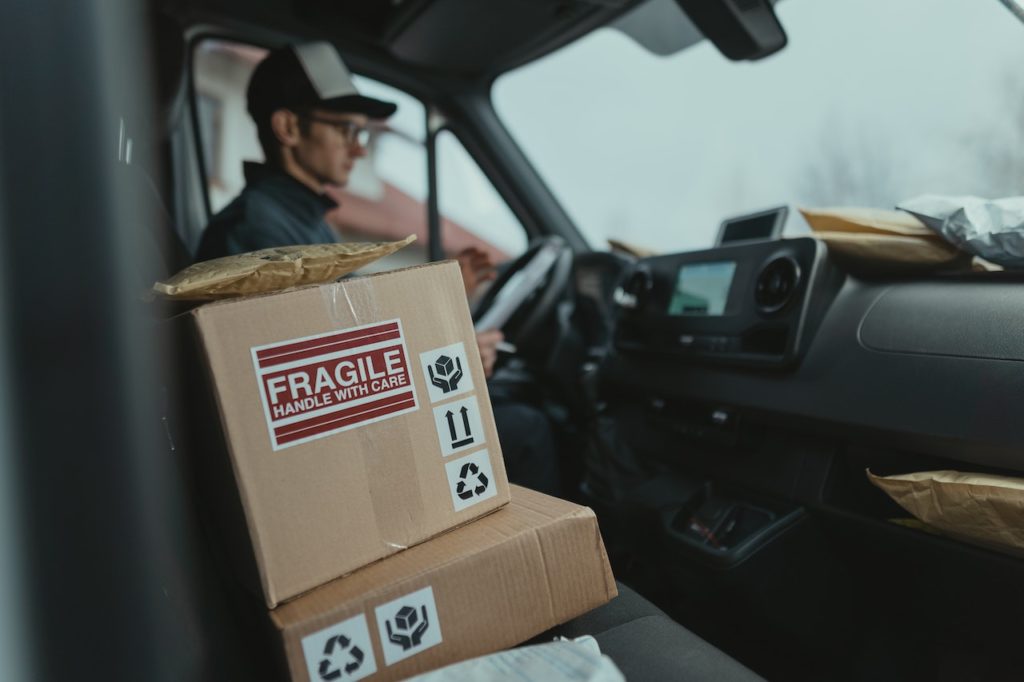Cardboard box with “fragile” sticker on it inside a truck with a driver in the background