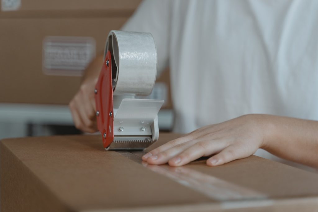 A person applying tape to a corrugated cardboard box