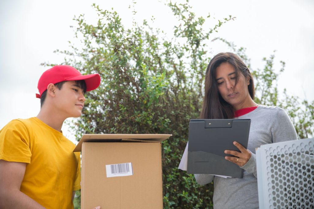 A delivery guy holding a cardboard box waiting for a woman to sign the delivery documents